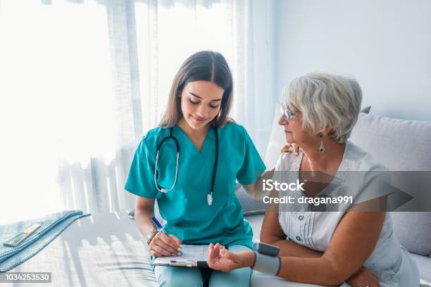 Nurse Measuring Blood Pressure Of Senior Woman At Home Stock Photo - Download Image Now