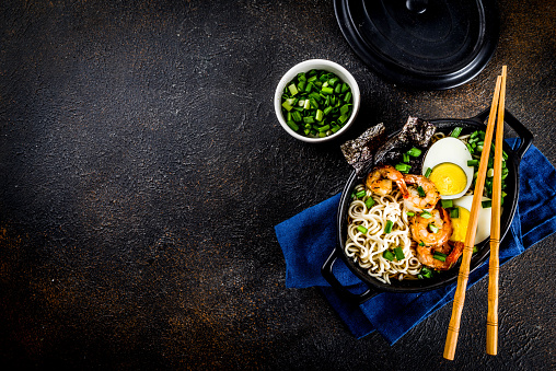 Traditional asian food, ramen soup with shrimp, noodles, spring onion, sliced eggs, mushrooms, on dark concrete background with chopsticks copy space top view