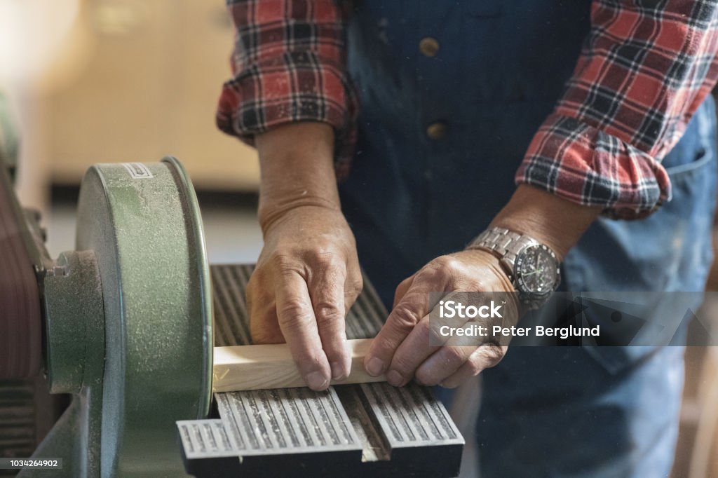 Man sanding a piece of wood A man is using a machine to sand a piece of wood. The photo is a close-up of his hands and the machine. Adult Stock Photo