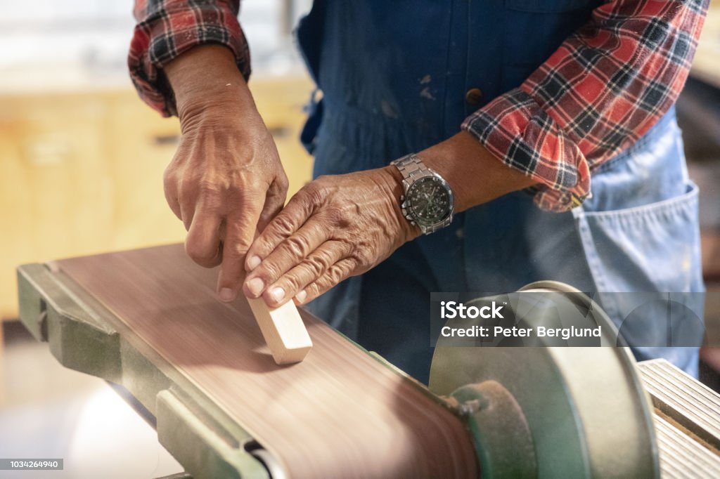 Man sanding a piece of wood A man is using a machine to sand a piece of wood. The photo is a close-up of his hands and the machine. Construction Worker Stock Photo