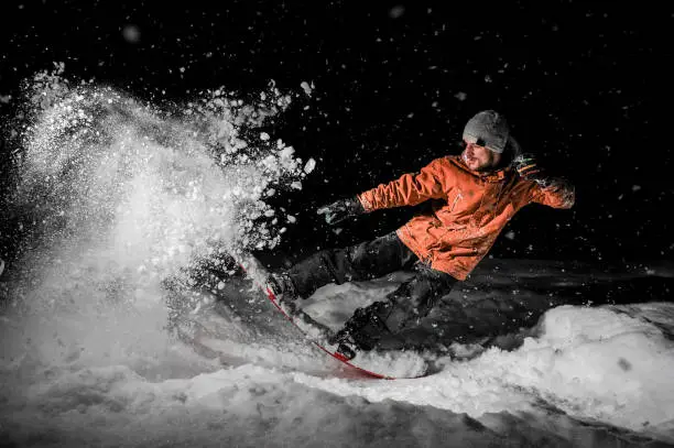 Photo of Young freeride snowboarder jumping in snow at night