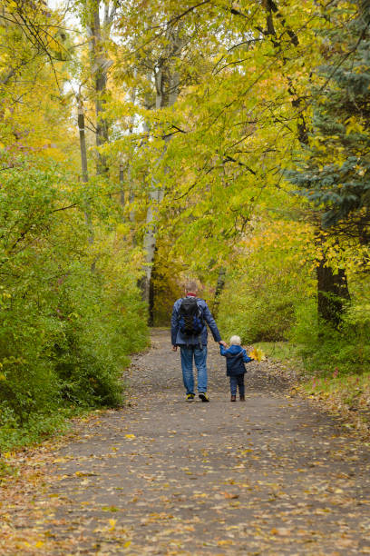 istock Father and son on their shoulders walk through the autumn park. Back view 1034275892