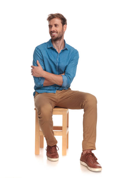 smiling seated young casual man looks to side smiling seated young casual man looks to side on white background sitting stock pictures, royalty-free photos & images
