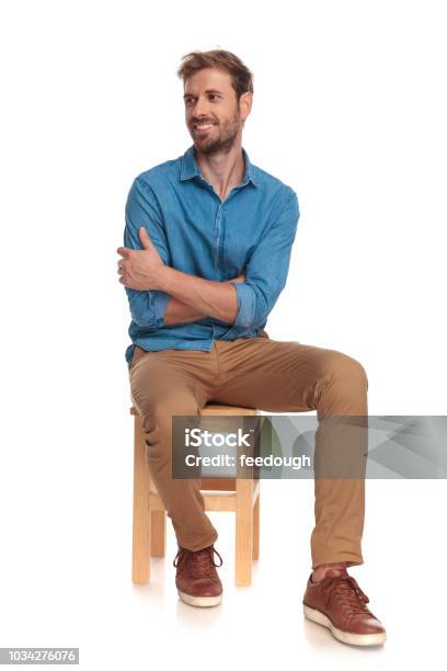 Smiling Seated Young Casual Man Looks To Side Stock Photo - Download Image Now - Sitting, Men, People
