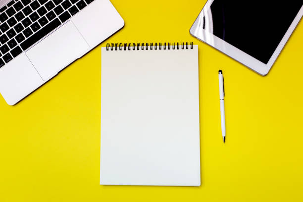 istock Yellow office desk table with  blank notebook, tablet, calculator and other office supplies. Top view with copy space. 1034279184