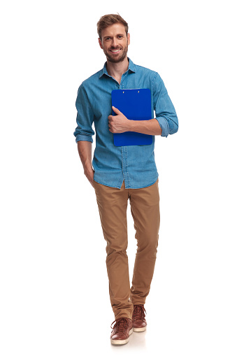 young casual student walks forward while holding notepad on white background