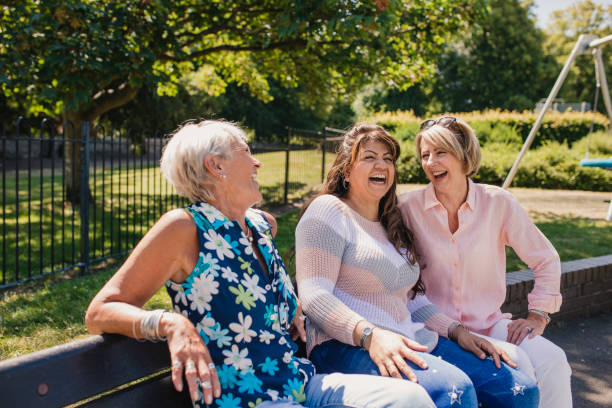 tres senior femenino riéndose en el parque - banco asiento fotografías e imágenes de stock