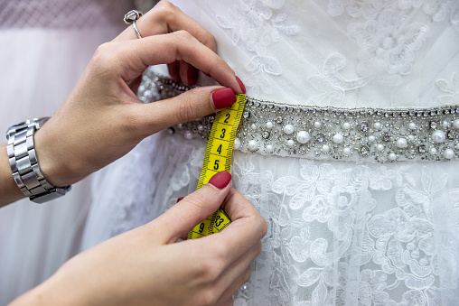 Measuring yellow tape with female hands and wedding dress