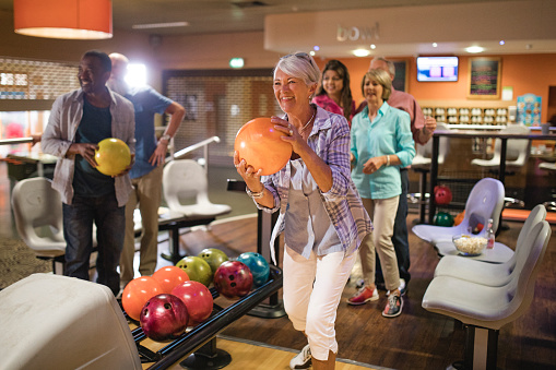 Group of seniors at a bowling alley, five senior friends can be seen in the background whilst a woman takes her turn.