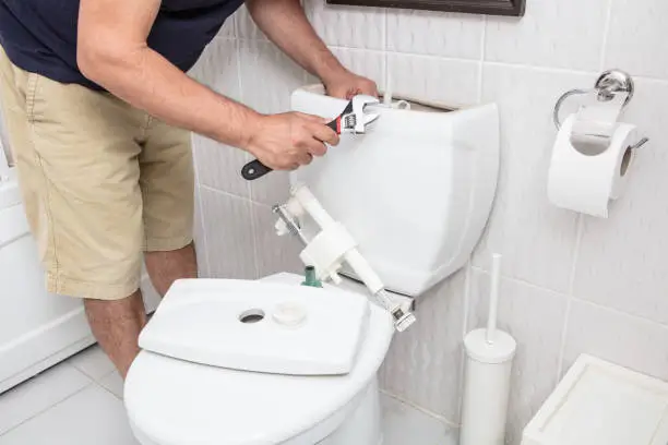 Man using wrench repairing toilet cistern in a concept of DIY repairs with copy space