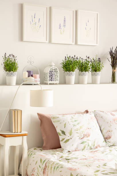 istock Lamp on table next to bed with patterned sheets in bedroom interior with flowers and posters. Real photo 1034329904