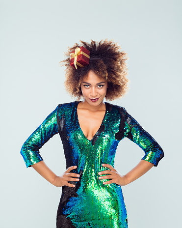 Portrait of beautiful african woman wearing sequined dress and funny headband looking at camera against white background.