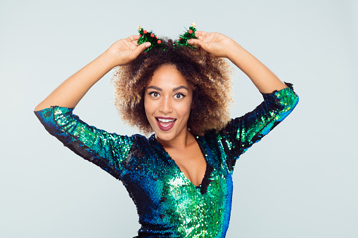 Portrait of beautiful african woman wearing sequined dress and funny headband staring at camera against white background.