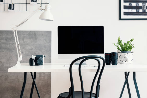 istock Black chair by a white desk with a computer and a lamp in a modern home office interior for a professional photographer freelancer. Real photo. 1034337690