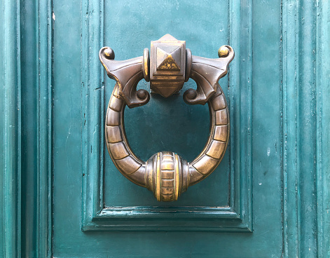 Weathered brass door knocker on teal painted door in Paris France.