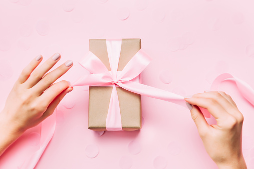 Beautiful woman hands with beautiful pastel manicure open gift box on pink trendy background. Holiday gift and trendy manicure concept.