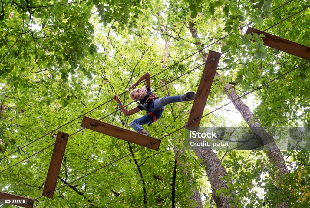 tree climbing adventure park From below looking up view. Young girl climbing the trees with help of ropes in an adventure park. Buckled up. Amusement Park Stock Photo