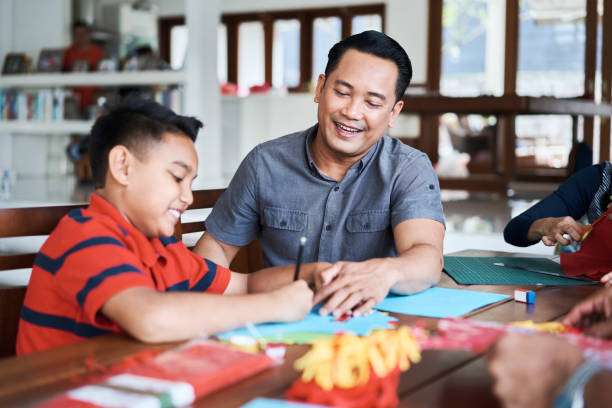 istock Father looking at son making Wau bulan at home 1034355860