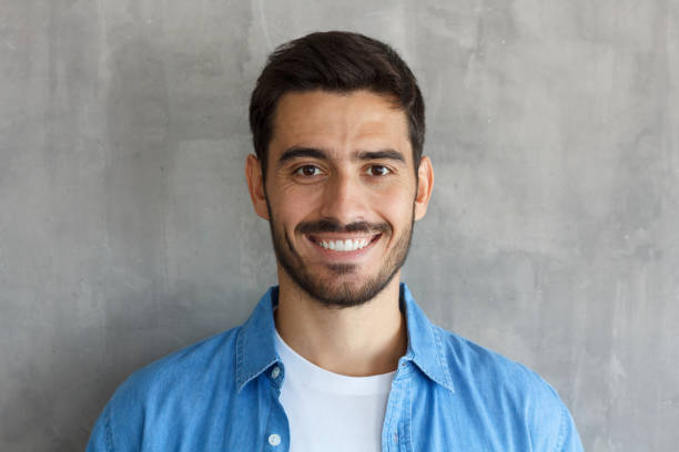 foto interior del europeo guapo chico foto aislada sobre fondo gris permanente cerca de la cámara con la cara morena de pelo y corte de pelo corto, mirada satisfecha y feliz, su tiempo de ocio - objeto masculino fotografías e imágenes de stock