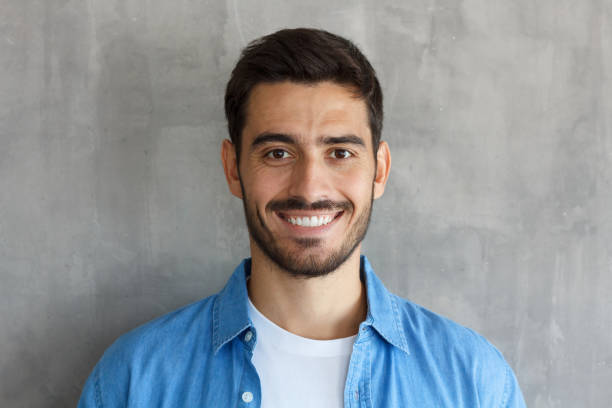 Indoor photo of handsome European guy pictured isolated on grey background standing close to camera with dark face hair and short haircut, looking satisfied and happy, spending his leisure time Indoor photo of handsome European guy pictured isolated on grey background standing close to camera with dark face hair and short haircut, looking satisfied and happy, spending his leisure time male likeness photos stock pictures, royalty-free photos & images