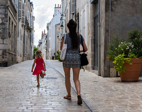 Orleans, France - August 11, 2018: Small alley with trunning child and walking woman and with old high houses with nostalgic lamps and plants in Orleans, France.