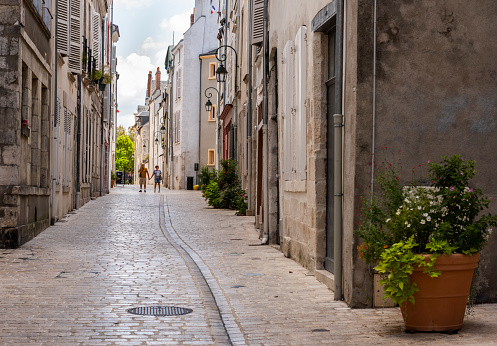 Orleans, France - August 11, 2018:  Small alley with tourists - man and woman hand in hand - and with old high houses with nostalgic lamps and plants in Orleans, France.