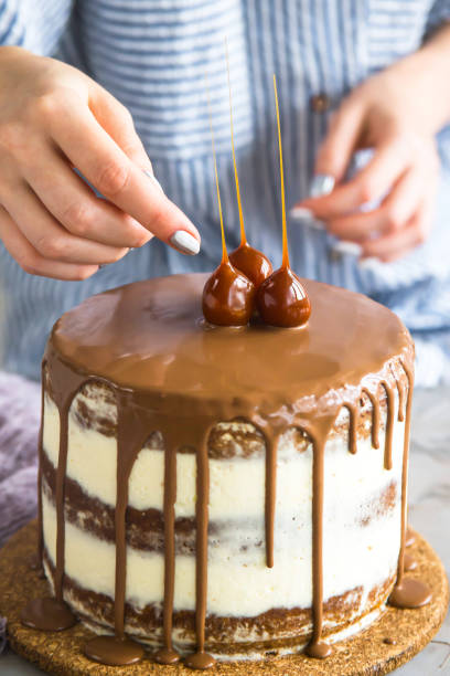 cukiernik dekoruje gotowe ciasto, wylane czekoladą, używając karmelowych ozdób. słodycze - choco zdjęcia i obrazy z banku zdjęć