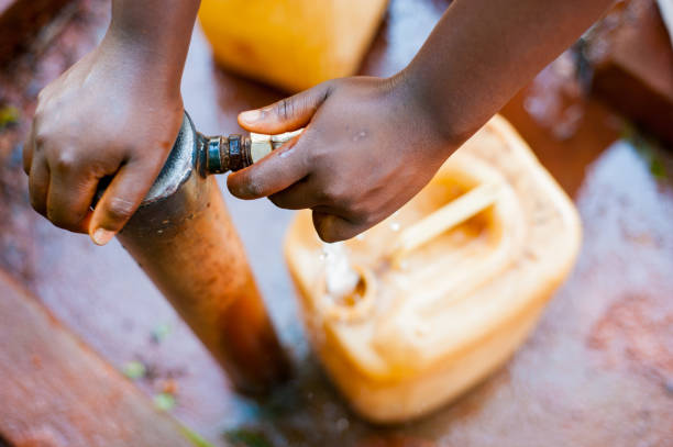above close view up of young african child hand filling tank with tap water with green background stock photo