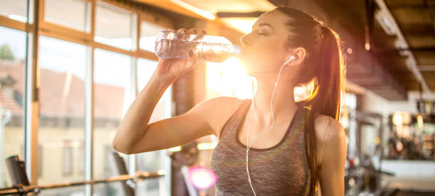 Side view panoramic profile of beautiful sporty girl with headphones drinking water during morning workout at gym Side view panoramic profile of beautiful sporty girl with headphones drinking water during morning workout at gym sport drink stock pictures, royalty-free photos & images