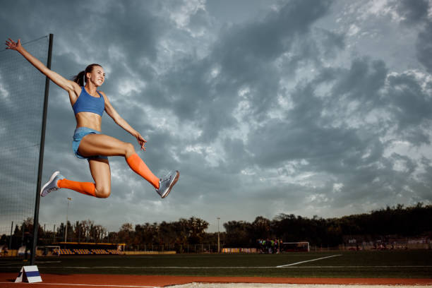 mujer atleta realizando un salto de longitud durante una competición - track and field athlete women vitality speed fotografías e imágenes de stock