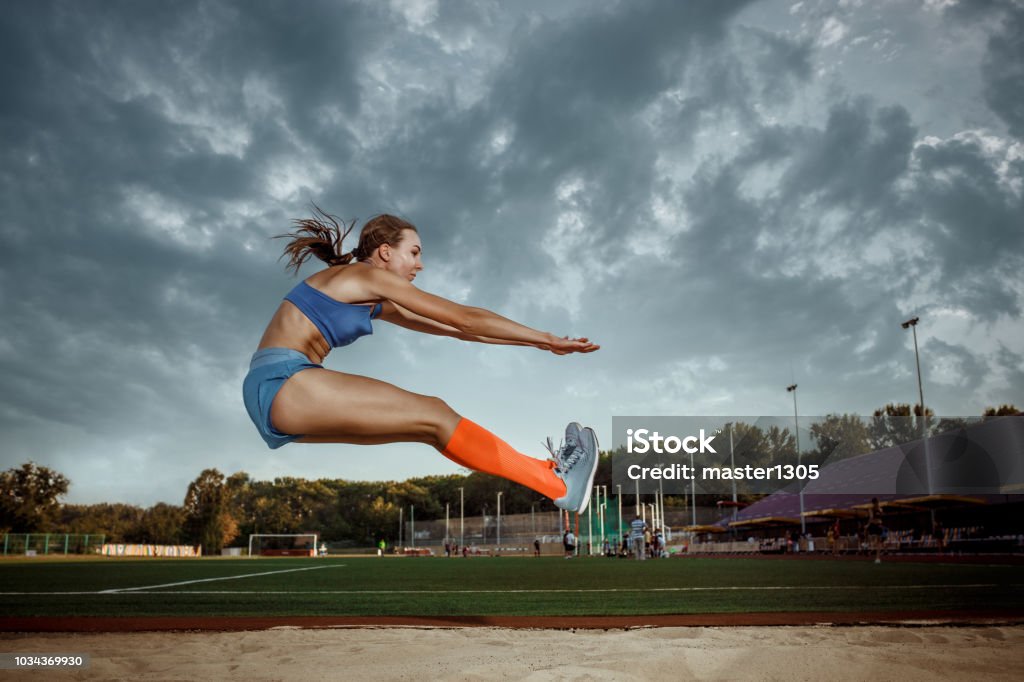 Female athlete performing a long jump during a competition Female athlete performing a long jump during a competition at stadium. The jump, athlete, action, motion, sport, success, championship concept Jumping Stock Photo
