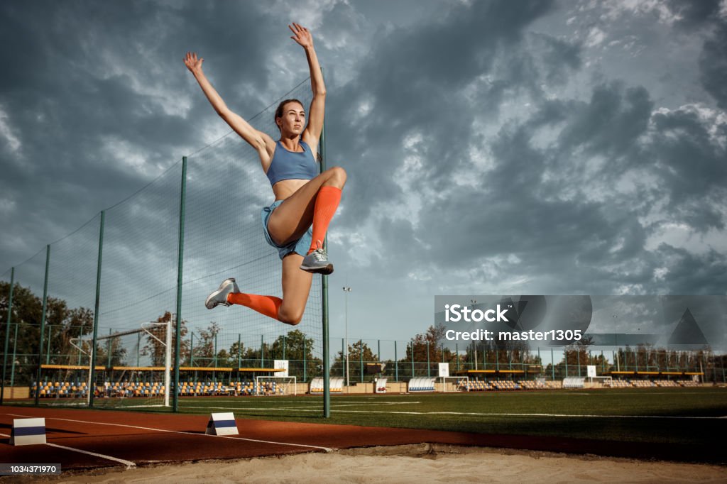 Female athlete performing a long jump during a competition Female athlete performing a long jump during a competition at stadium. The jump, athlete, action, motion, sport, success, championship concept Sand Trap Stock Photo