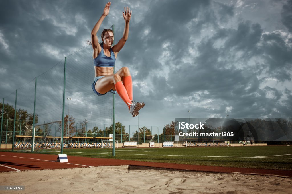 Female athlete performing a long jump during a competition Female athlete performing a long jump during a competition at stadium. The jump, athlete, action, motion, sport, success, championship concept Adult Stock Photo