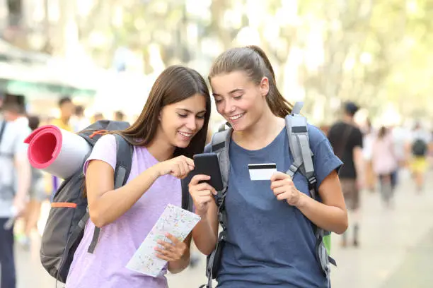 Two happy backpackers searching online content in a smart phone in the street