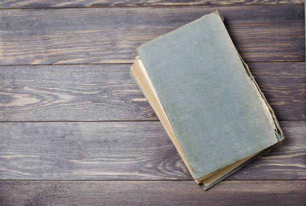 istock An old book with a torn cover. Wooden background. Flat top view 1034376778