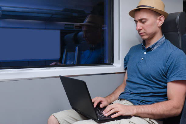 istock Young man in hat working behind a laptop sitting in a train chair 1034383606