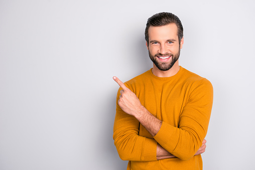 Portrait of cheerful handsome attractive bearded brutal fashionable modern stylish macho toothy beaming smile wearing tight sweater pointing on copy-space empty blank space isolated on gray background