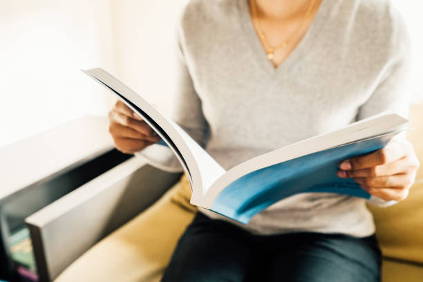istock Young asian woman sitting on a sofa opening book while reading at home or library, education concept background 1034387782