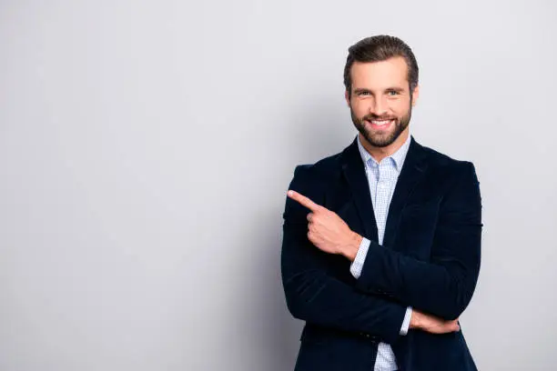 Photo of Portrait of cheerful excited joyful satisfied handsome attractive fashionable macho guy dressed in formal outfit dark velvet pointing on empty blank copyspace isolated on gray background copy-space