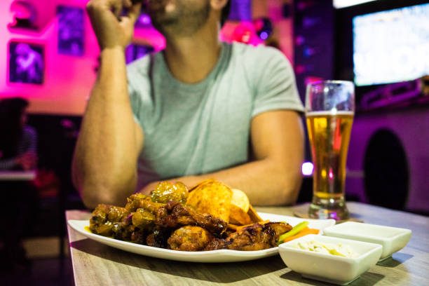 Man of Latin race, between 20 and 30 years old, enjoy a delicious piece of chicken, with a beer, sitting at the table of a bar - restaurant