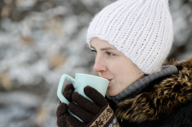 istock Girl in winter clothes drinking tea from a mug, side view, close-up 1034408572