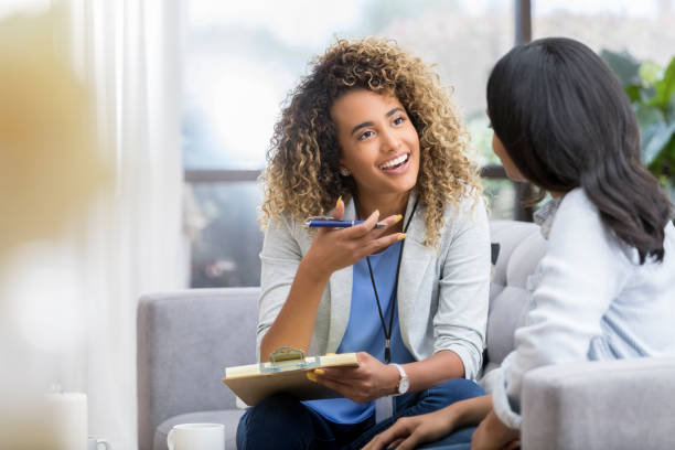 Encouraging therapist talks with young woman Positive young female therapist gestures as she talks with a female client. The therapist smiles warmly as she talks with the young woman. psychotherapy stock pictures, royalty-free photos & images