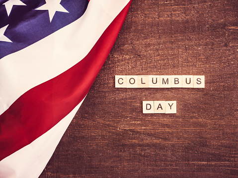 Wooden letters of the alphabet in the form of the word Columbus Day against the background of the US flag and a vintage wooden surface. Top view, close-up