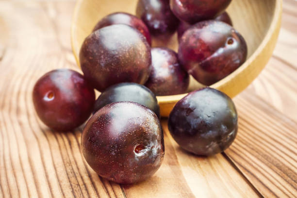 istock Plums scattered from wooden bowl on the table. 1034438000