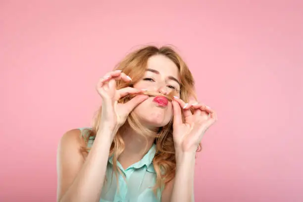 funny amusing laughable girl monkeying around with her hair. portrait of a young carefree woman making a mustache with her locks on pink background.