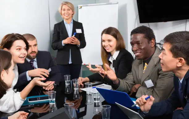 Cheerful positive glad mature businesswoman discussing new project with his team in meeting room