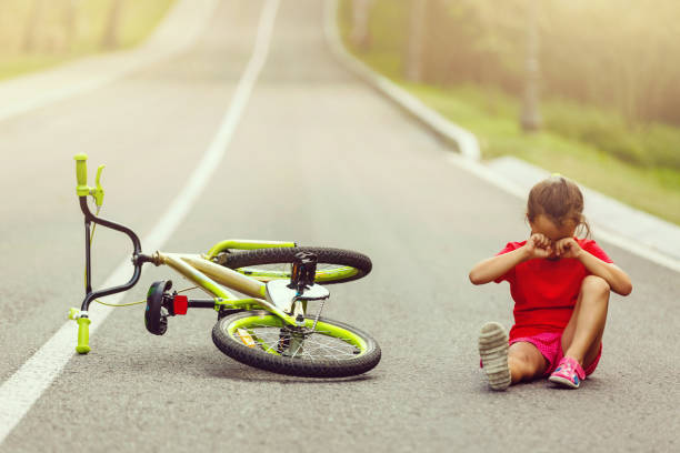 a little girl riding a bicycle. the bike accident. sit crying on the street - helmet bicycle little girls child imagens e fotografias de stock