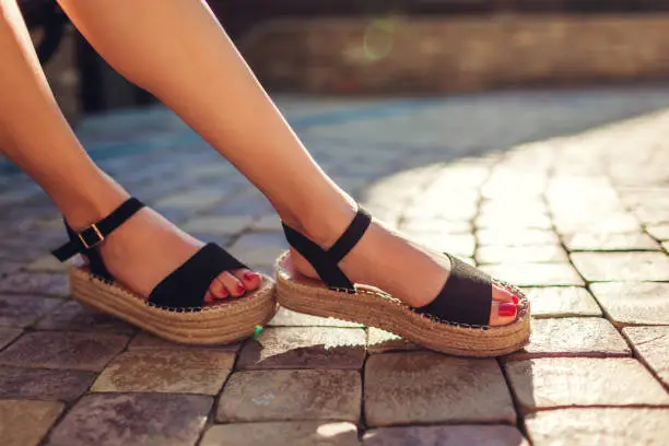 Photo of Stylish woman wearing black summer shoes with straw sole outdoors. Comfortable sandals. Beauty fashion.