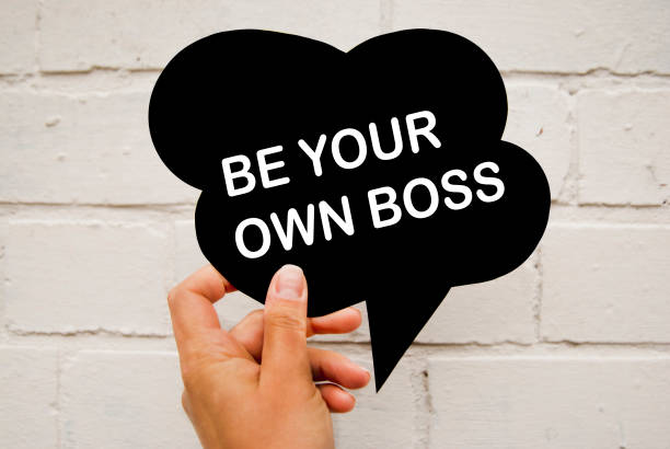 istock Hand holding black paper speech bubble with BE YOUR BOSS concept, over white brick wall background, isolated. Business Concept. 1034461946