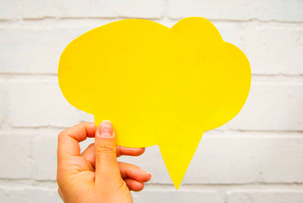 istock Hand holding an empty yellow hand-cuted paper speech bubble on white textured brick wall background. Isolated. 1034461990